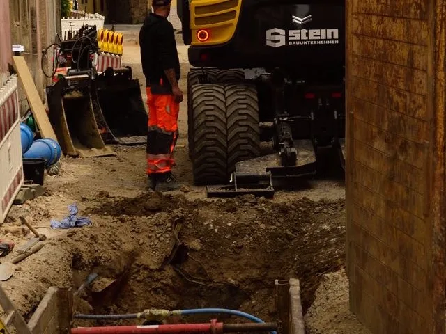 Nyitott csővezeték-árok kotrógéppel és lefektetett műanyag csövekkel egy városi utcán